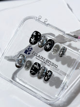 Black and silver press-on nails with 3D chrome swirl accents, star details, and shimmer gradient in a bold winter aesthetic.
