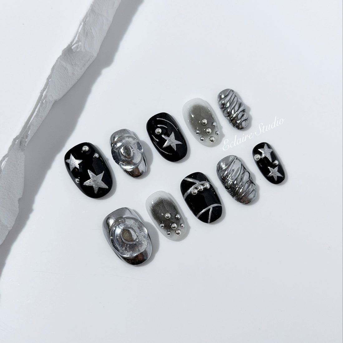 Black and silver press-on nails with 3D chrome swirl accents, star details, and shimmer gradient in a bold winter aesthetic.
