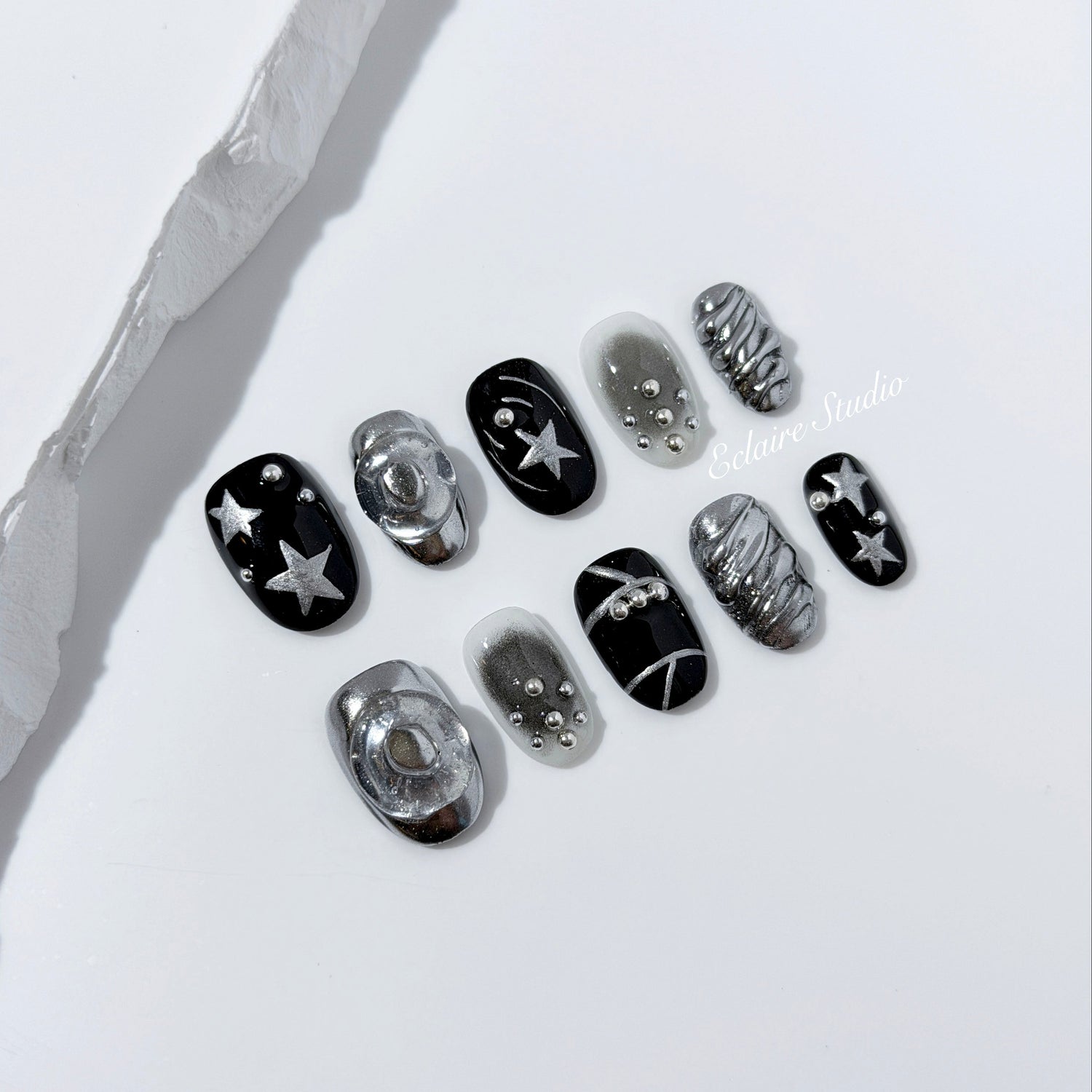 Black and silver press-on nails with 3D chrome swirl accents, star details, and shimmer gradient in a bold winter aesthetic.
