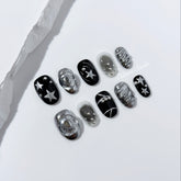 Black and silver press-on nails with 3D chrome swirl accents, star details, and shimmer gradient in a bold winter aesthetic.
