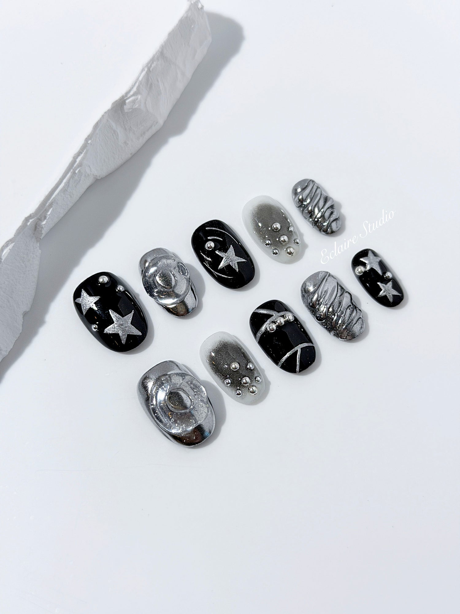 Black and silver press-on nails with 3D chrome swirl accents, star details, and shimmer gradient in a bold winter aesthetic.

