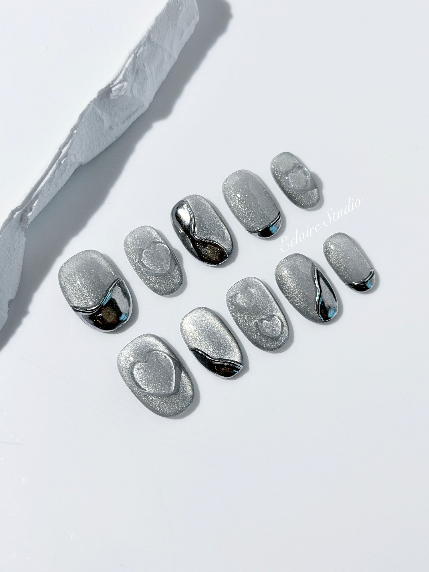 Extra short silver cat-eye press-on nails with chrome ripple accents and 3D heart details, minimalist winter aesthetic.
