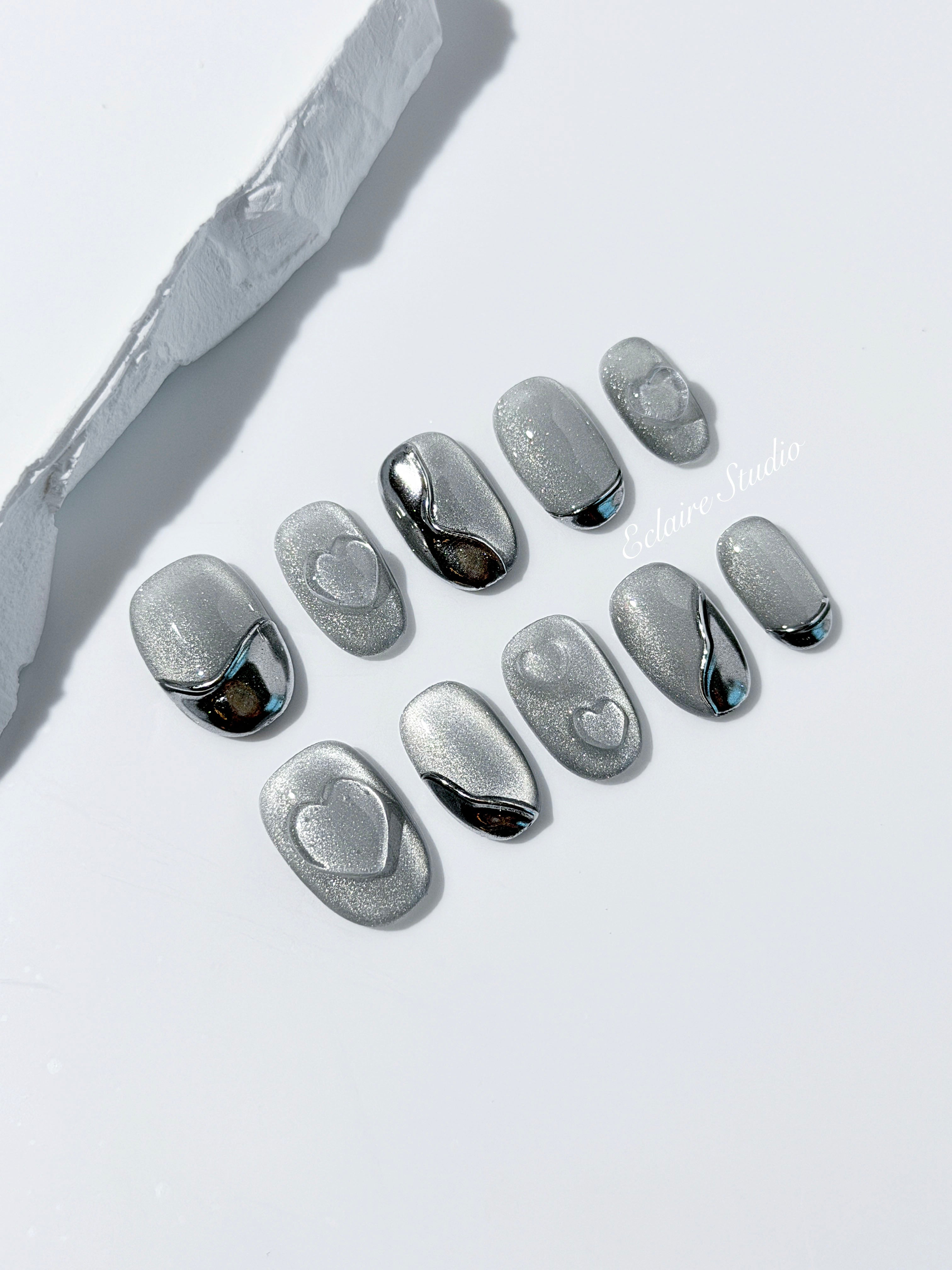 Extra short silver cat-eye press-on nails with chrome ripple accents and 3D heart details, minimalist winter aesthetic.
