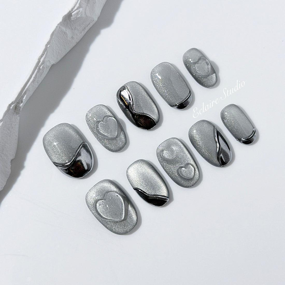 Extra short silver cat-eye press-on nails with chrome ripple accents and 3D heart details, minimalist winter aesthetic.
