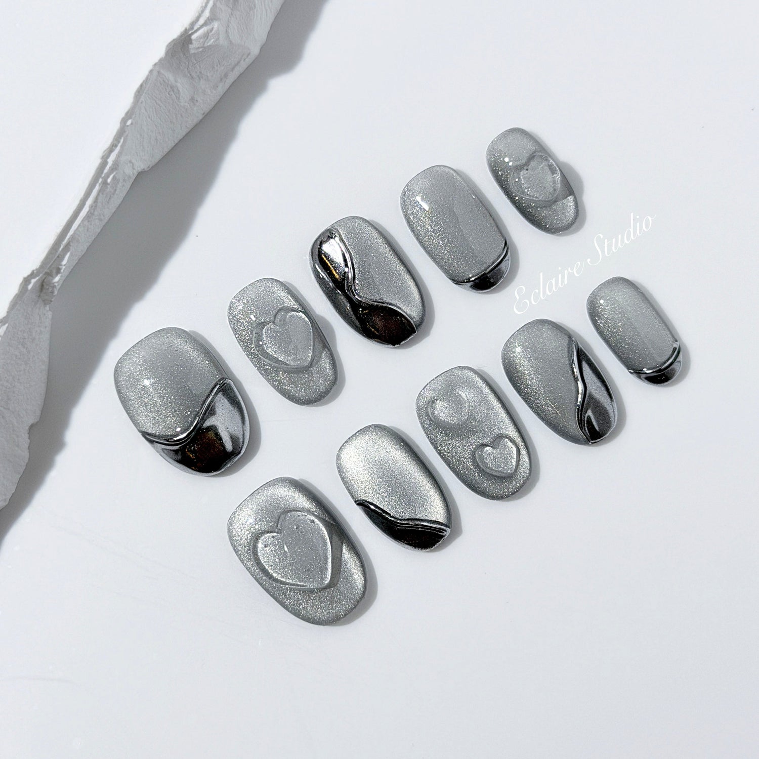 Extra short silver cat-eye press-on nails with chrome ripple accents and 3D heart details, minimalist winter aesthetic.
