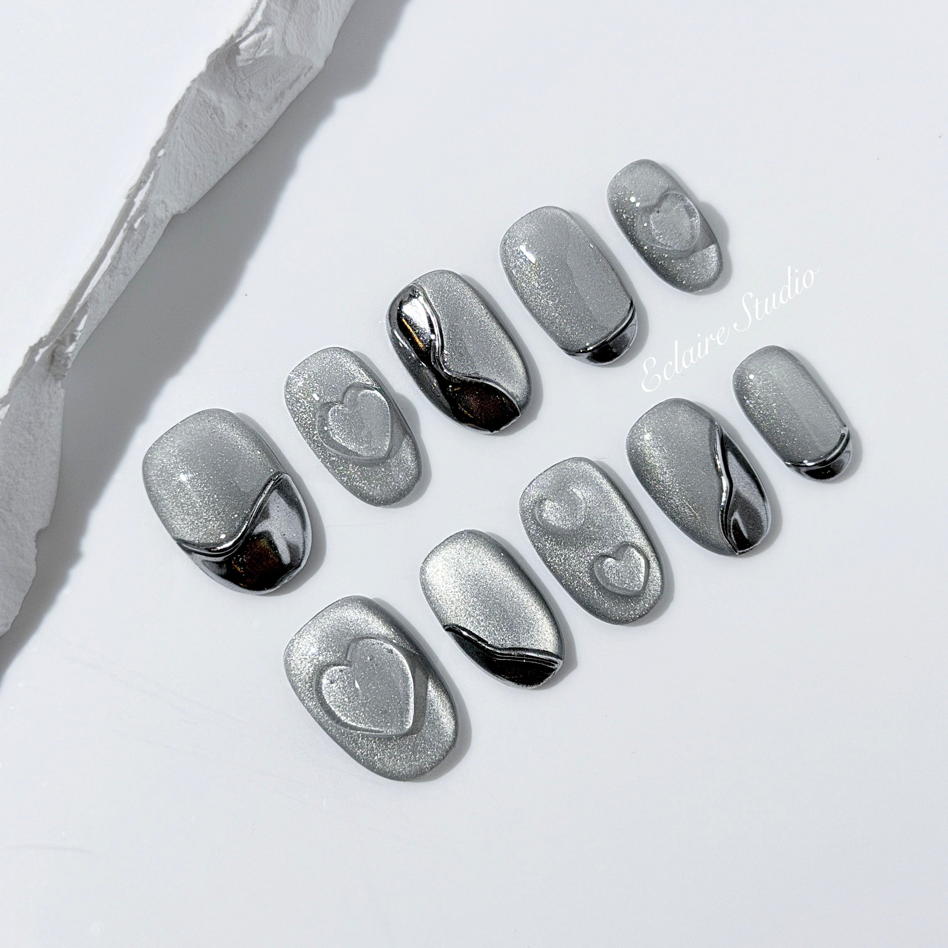 Extra short silver cat-eye press-on nails with chrome ripple accents and 3D heart details, minimalist winter aesthetic.
