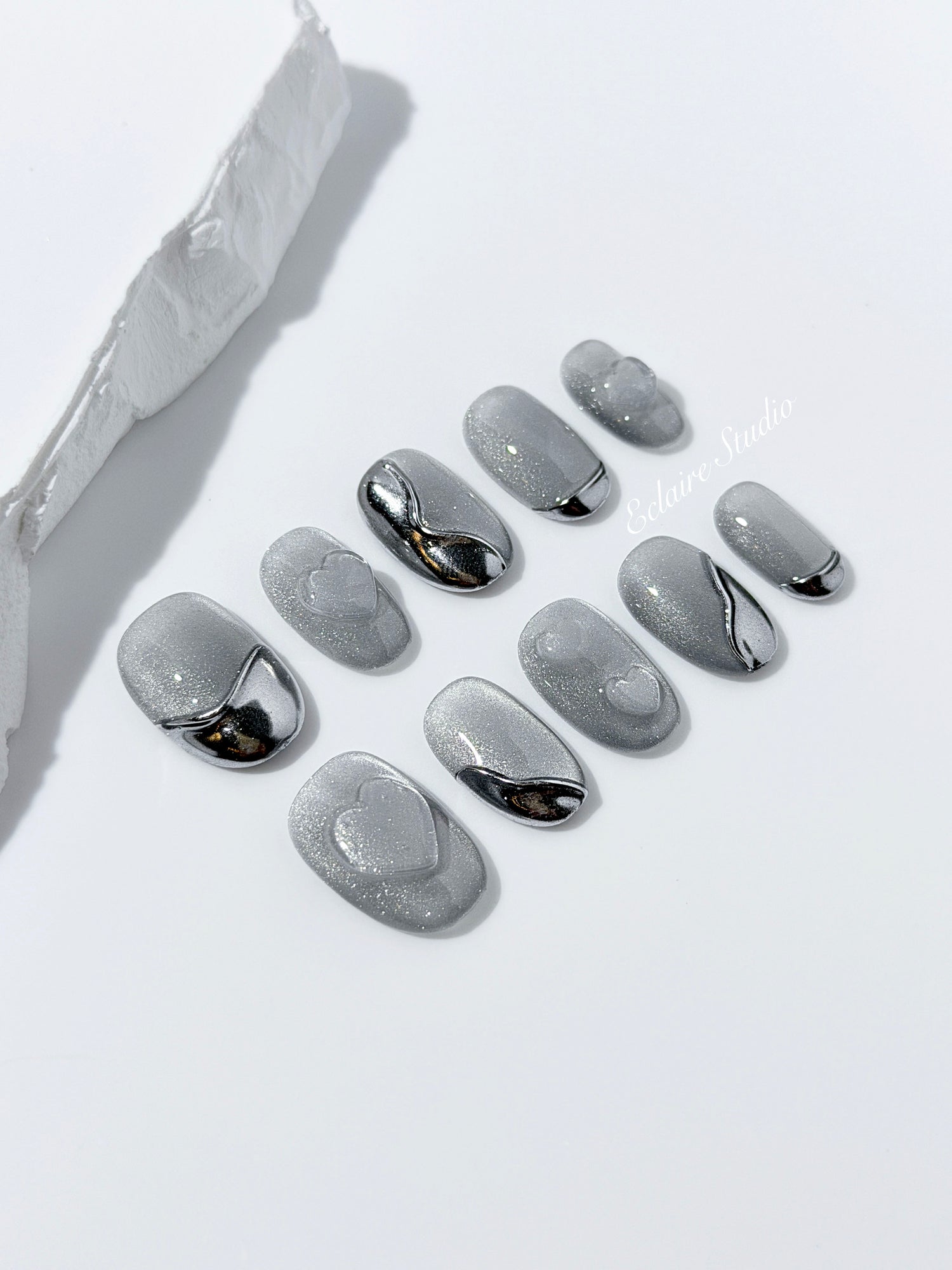 Extra short silver cat-eye press-on nails with chrome ripple accents and 3D heart details, minimalist winter aesthetic.
