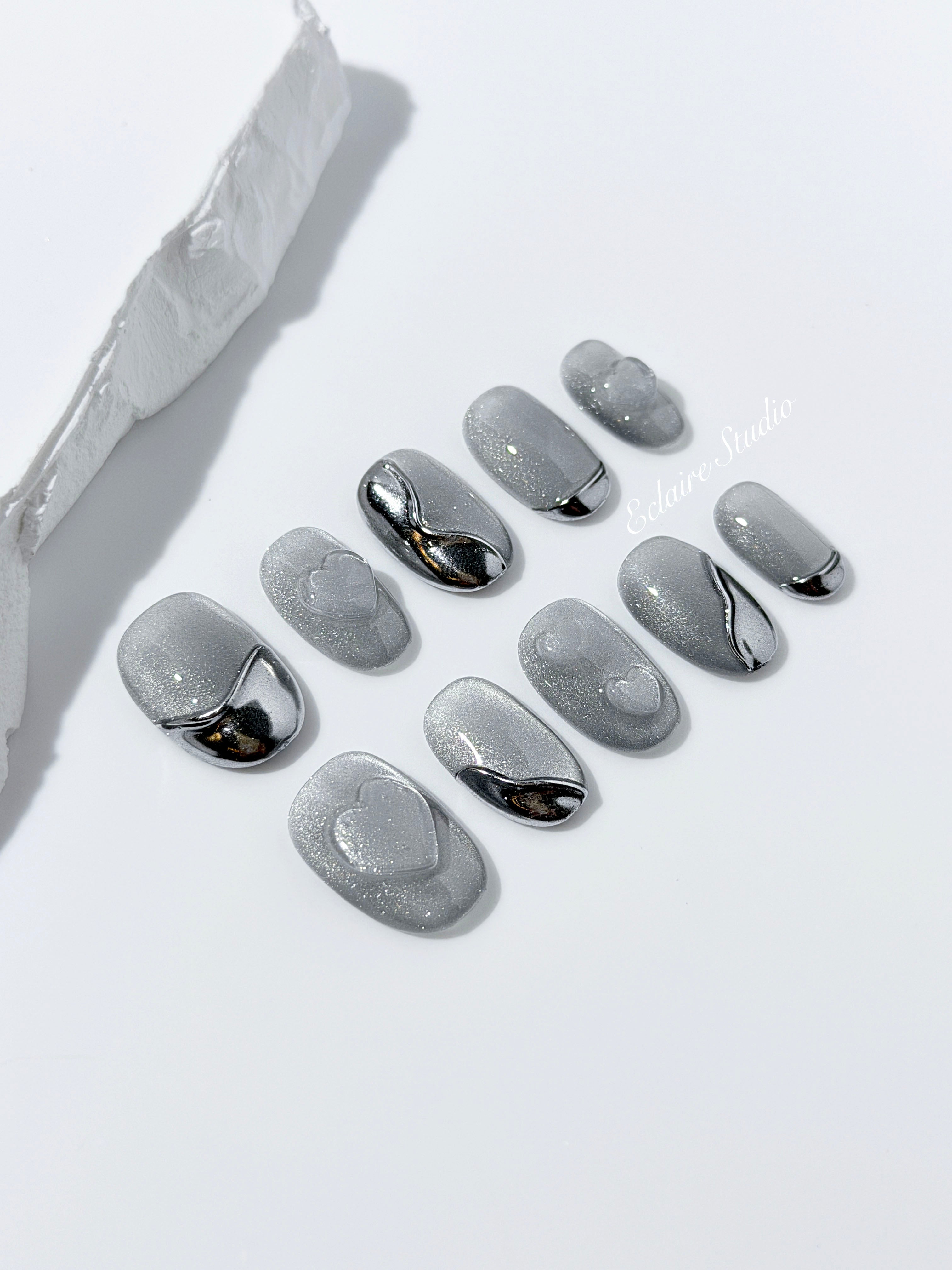 Extra short silver cat-eye press-on nails with chrome ripple accents and 3D heart details, minimalist winter aesthetic.
