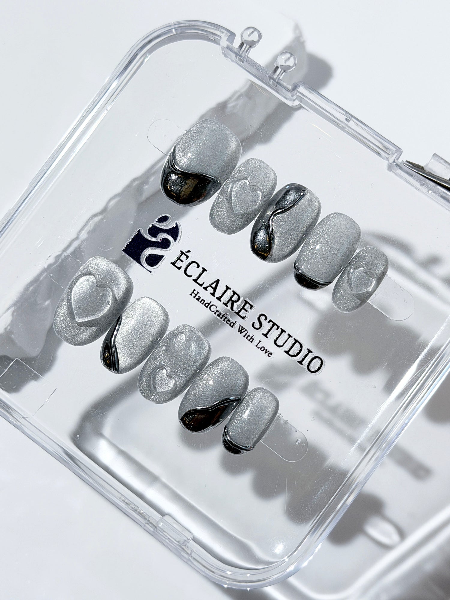 Extra short silver cat-eye press-on nails with chrome ripple accents and 3D heart details, minimalist winter aesthetic.
