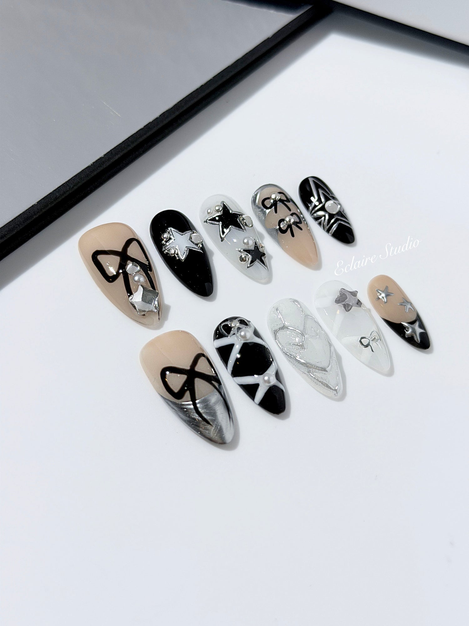 Handmade black, white, and nude press-on nails featuring bows, star charms, and pearl embellishments.