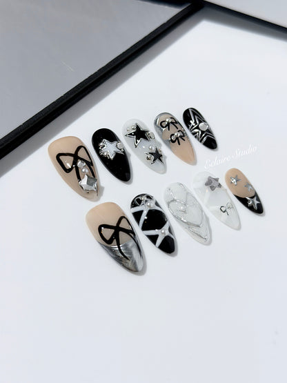 Handmade black, white, and nude press-on nails featuring bows, star charms, and pearl embellishments.