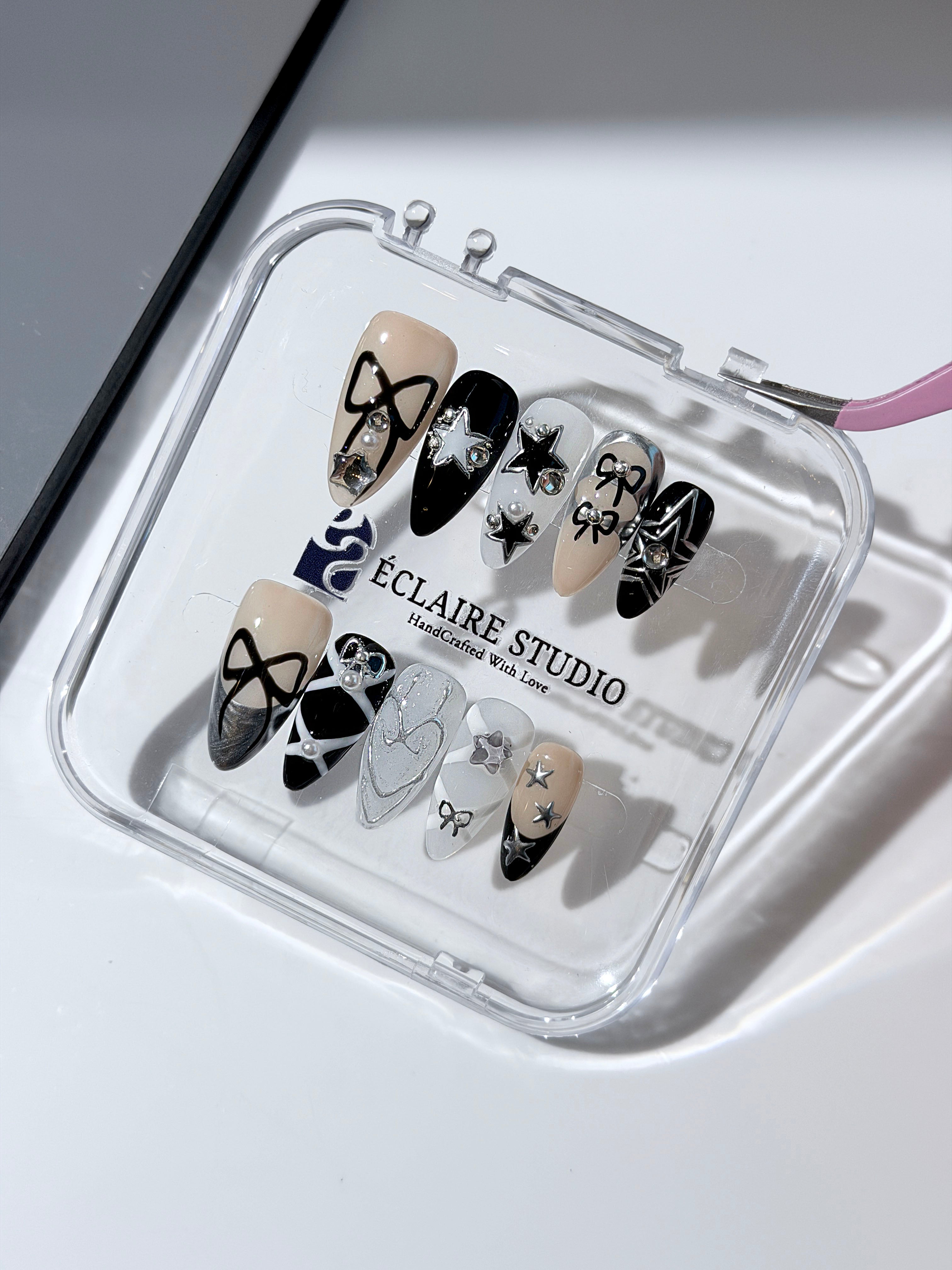 Handmade black, white, and nude press-on nails featuring bows, star charms, and pearl embellishments.