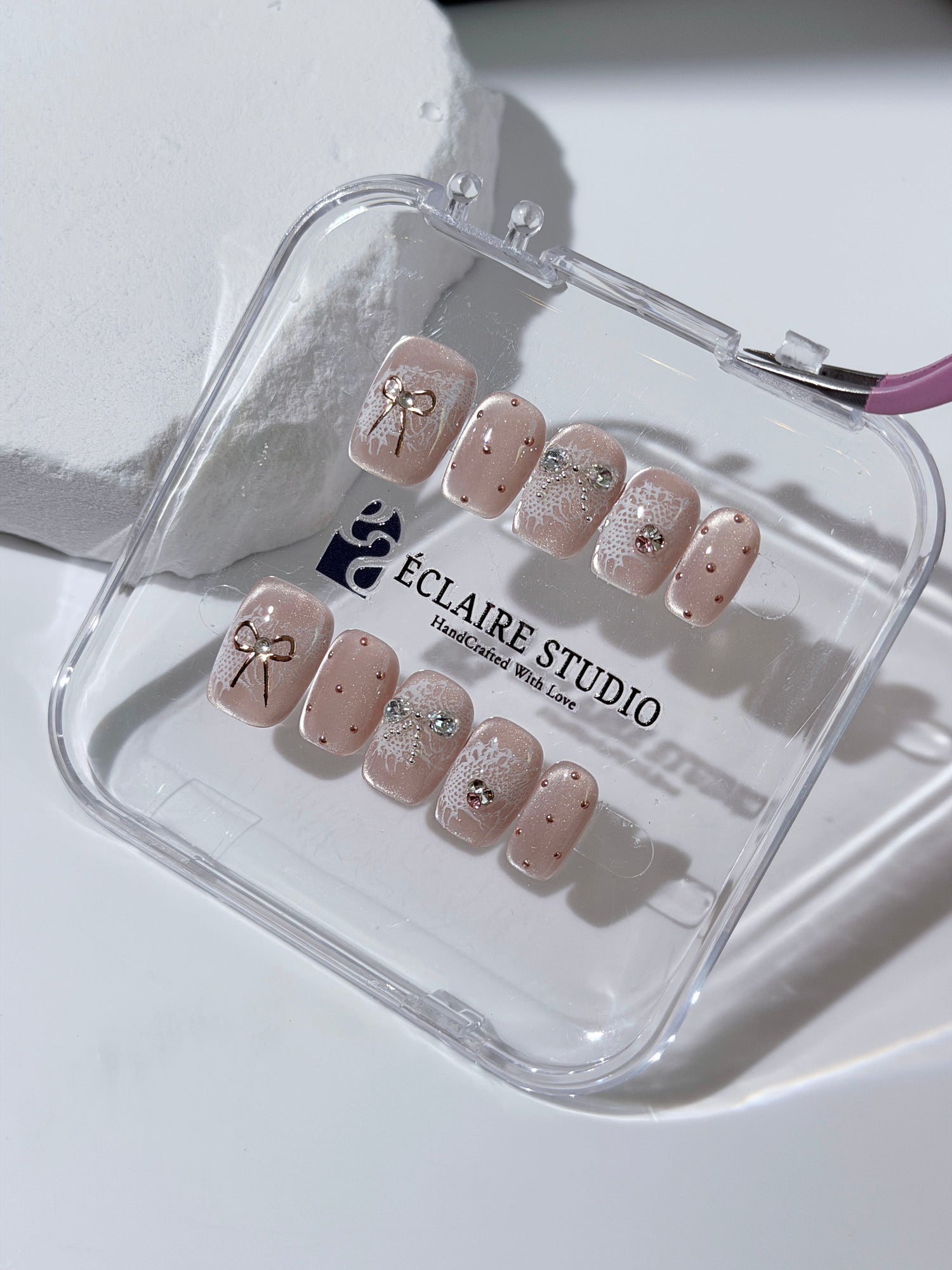 Short coffin pink nude cat-eye press-on nails with lace texture and pearl bow accents in a soft romantic winter style.
