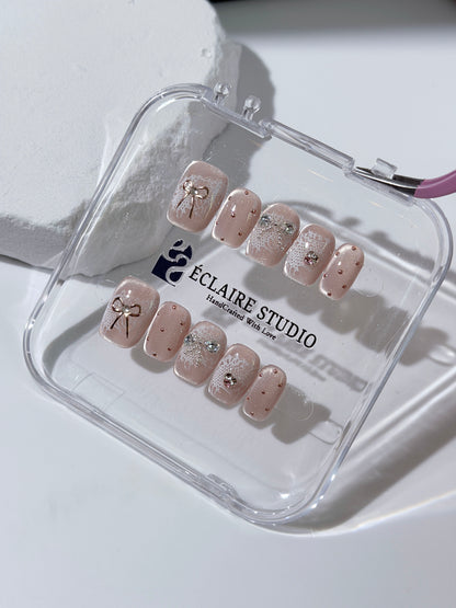 Short coffin pink nude cat-eye press-on nails with lace texture and pearl bow accents in a soft romantic winter style.
