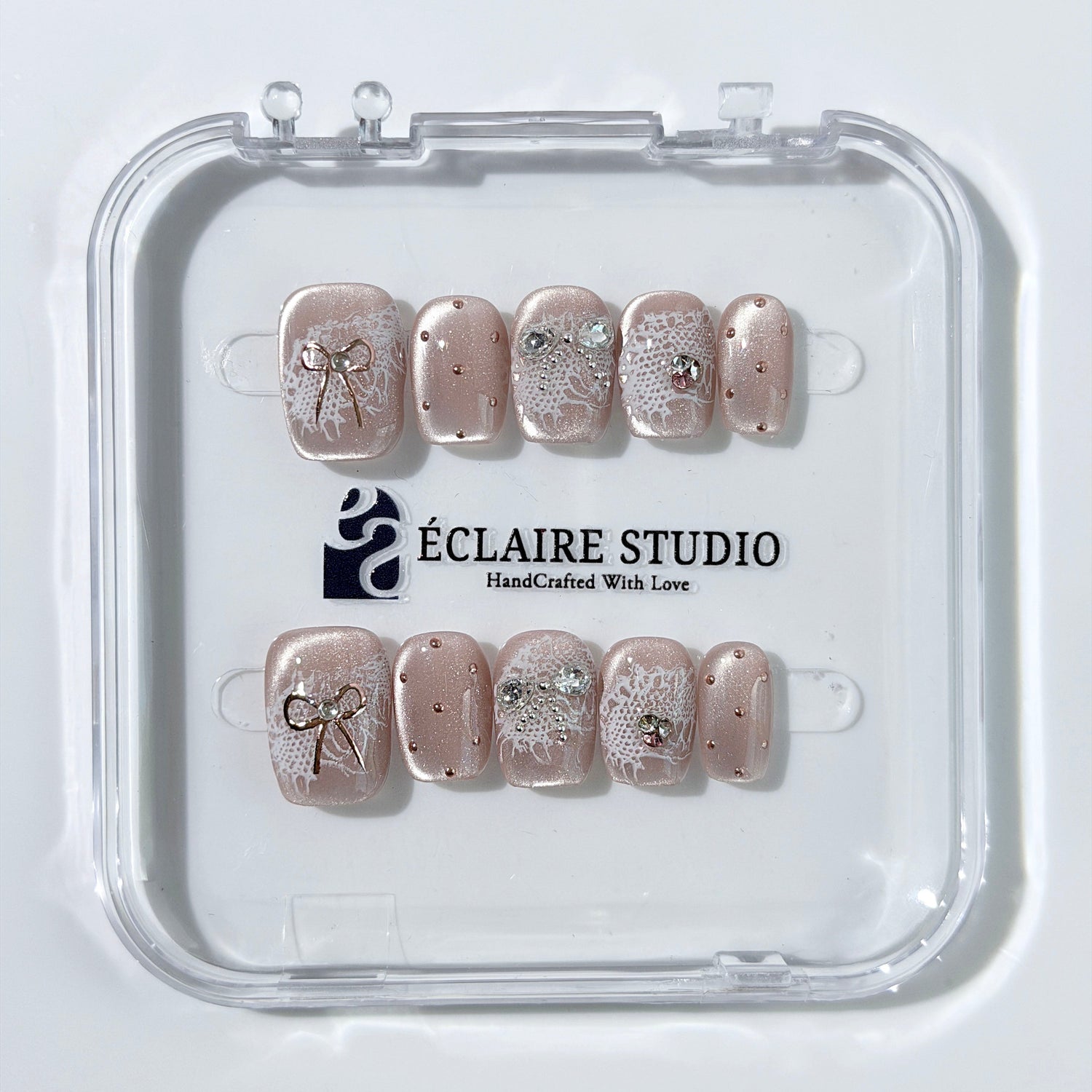 Short coffin pink nude cat-eye press-on nails with lace texture and pearl bow accents in a soft romantic winter style.
