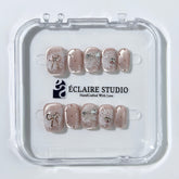 Short coffin pink nude cat-eye press-on nails with lace texture and pearl bow accents in a soft romantic winter style.
