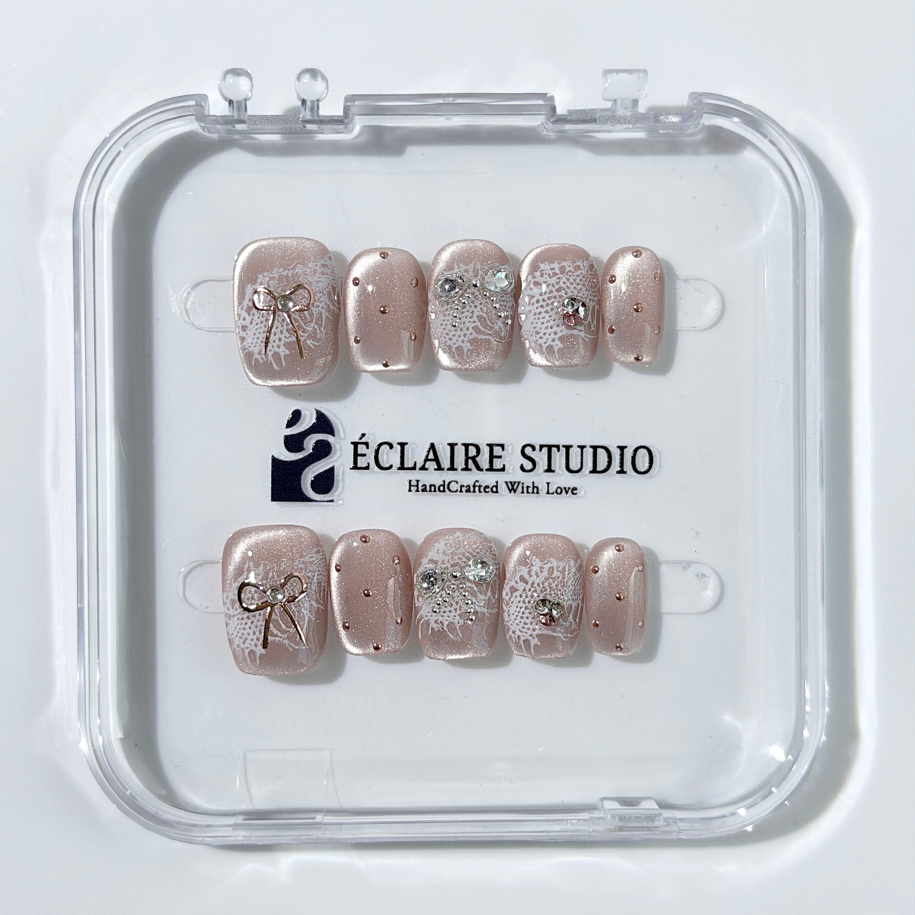 Short coffin pink nude cat-eye press-on nails with lace texture and pearl bow accents in a soft romantic winter style.
