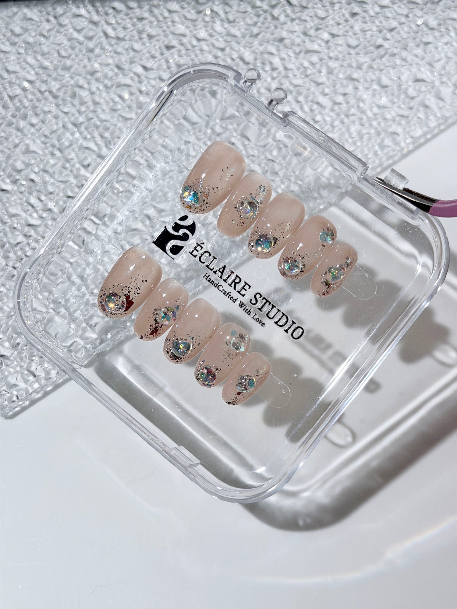 Short milky nude press-on nails with iridescent glitter and 3D crystal droplets, soft winter sugar aesthetic.
