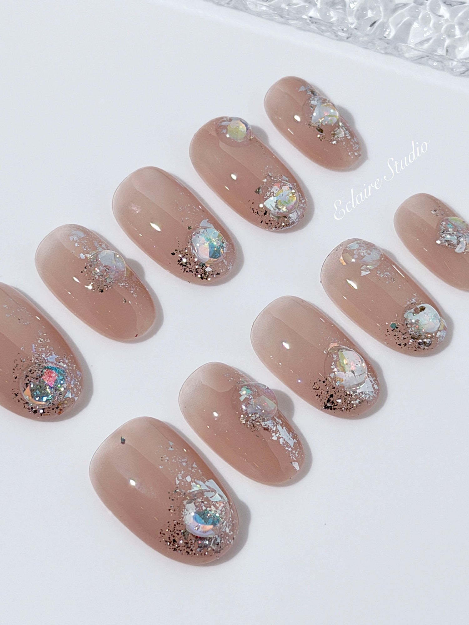 Short milky nude press-on nails with iridescent glitter and 3D crystal droplets, soft winter sugar aesthetic.
