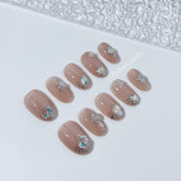 Short milky nude press-on nails with iridescent glitter and 3D crystal droplets, soft winter sugar aesthetic.
