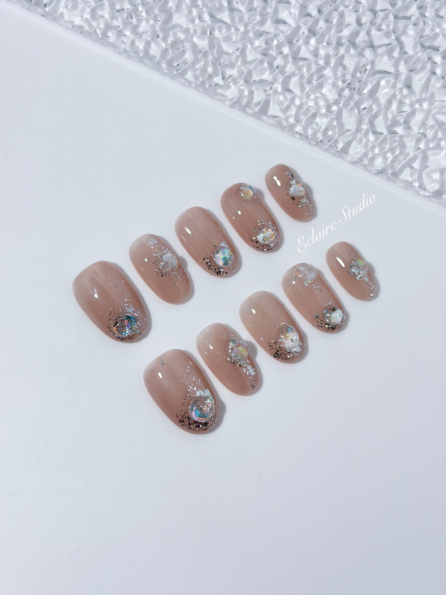 Short milky nude press-on nails with iridescent glitter and 3D crystal droplets, soft winter sugar aesthetic.
