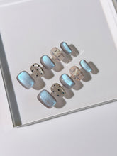 Pastel blue cat-eye press-on nails with glitter accents and 3D clear star details in a soft winter sorbet aesthetic.
