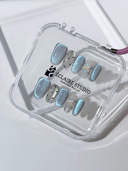Pastel blue cat-eye press-on nails with glitter accents and 3D clear star details in a soft winter sorbet aesthetic.
