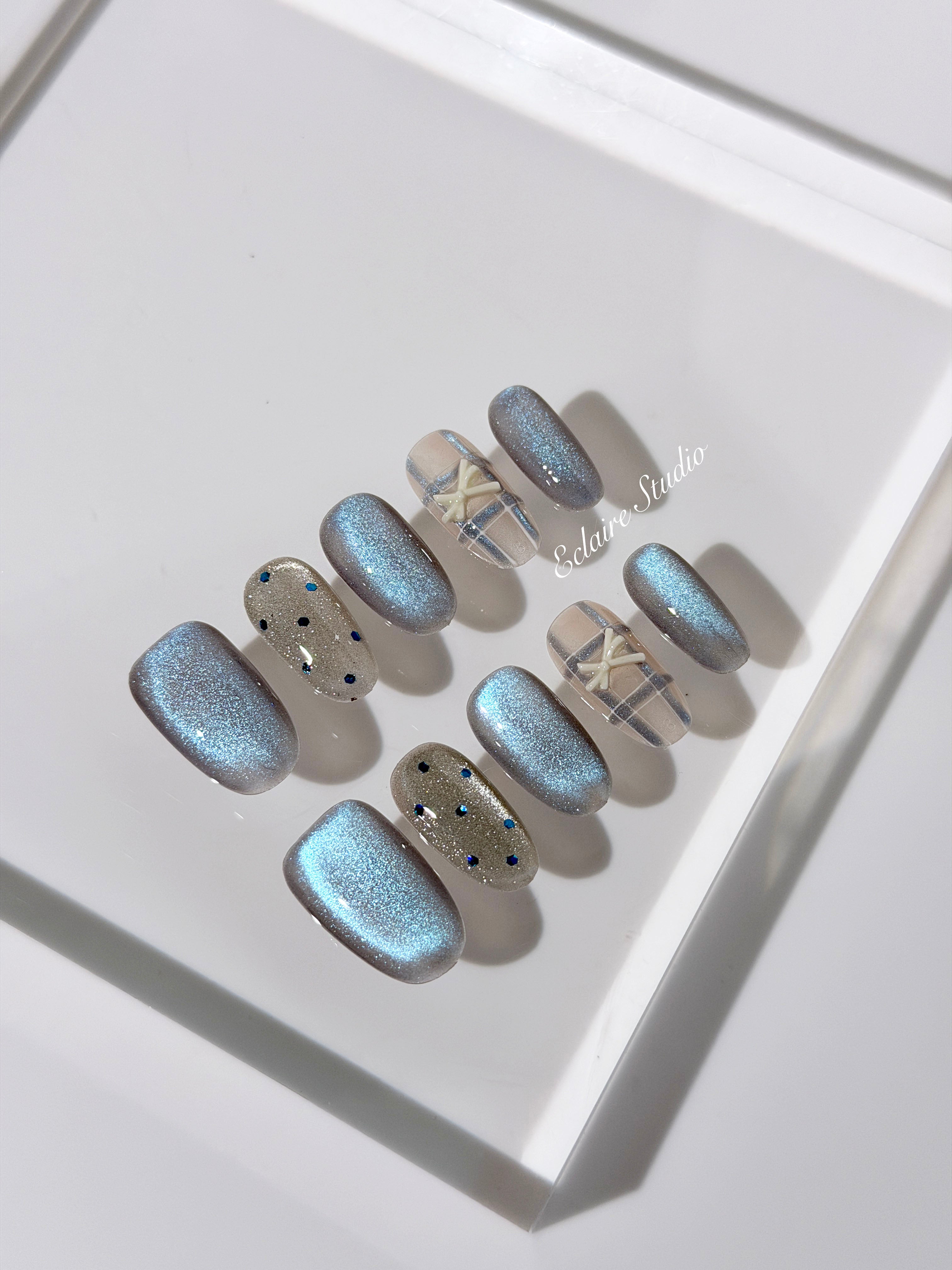 Pastel blue cat-eye press-on nails with glitter accents and 3D clear star details in a soft winter sorbet aesthetic.
