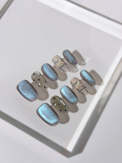 Pastel blue cat-eye press-on nails with glitter accents and 3D clear star details in a soft winter sorbet aesthetic.
