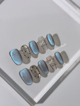 Pastel blue cat-eye press-on nails with glitter accents and 3D clear star details in a soft winter sorbet aesthetic.
