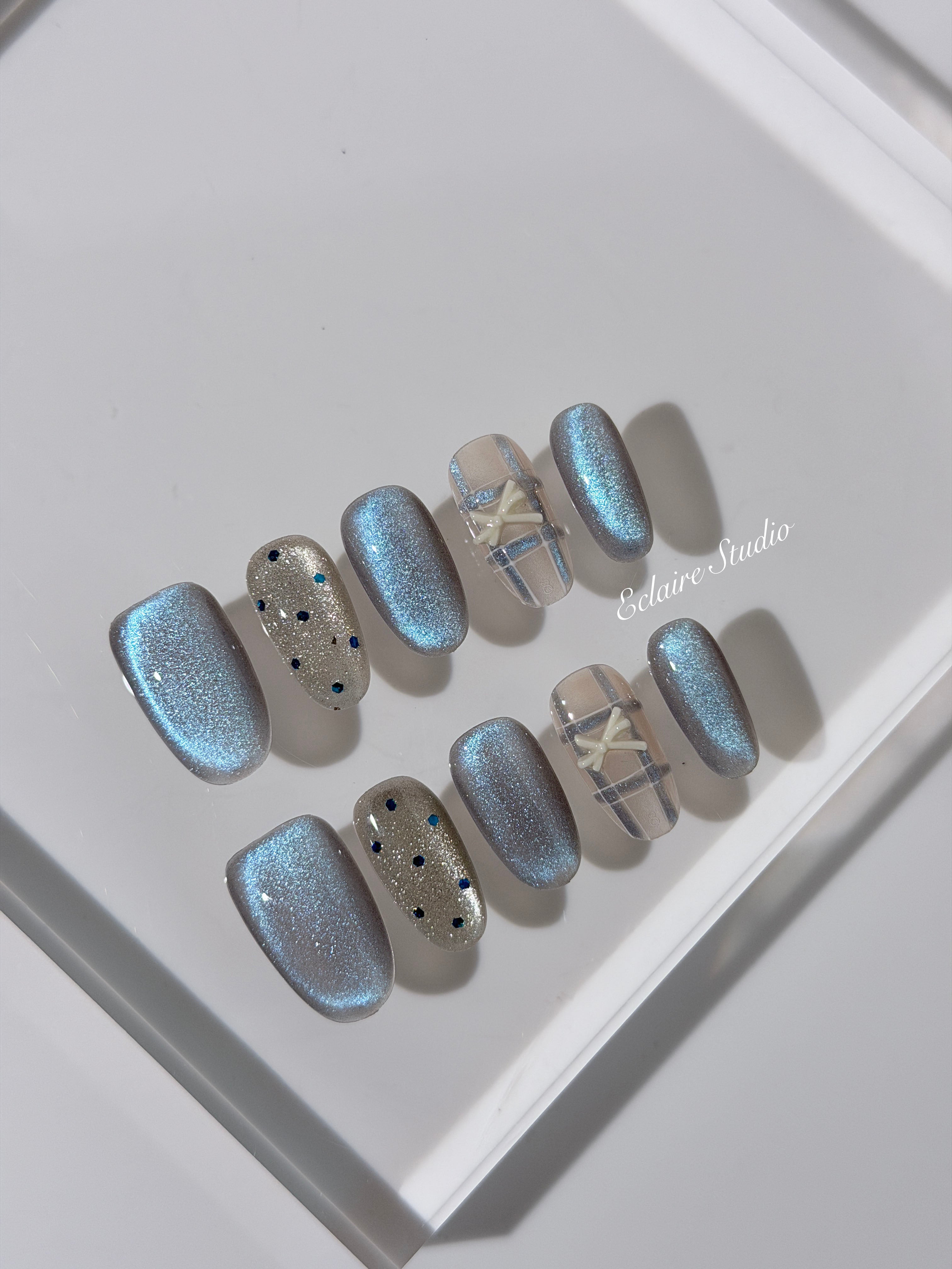 Pastel blue cat-eye press-on nails with glitter accents and 3D clear star details in a soft winter sorbet aesthetic.
