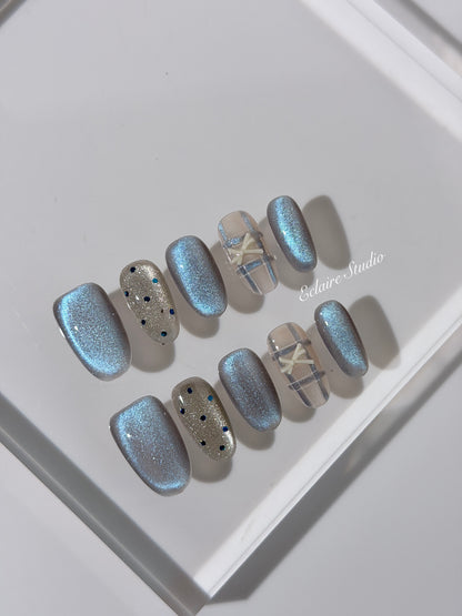 Pastel blue cat-eye press-on nails with glitter accents and 3D clear star details in a soft winter sorbet aesthetic.

