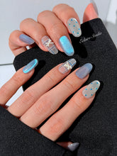 Pastel blue cat-eye press-on nails with glitter accents and 3D clear star details in a soft winter sorbet aesthetic.
