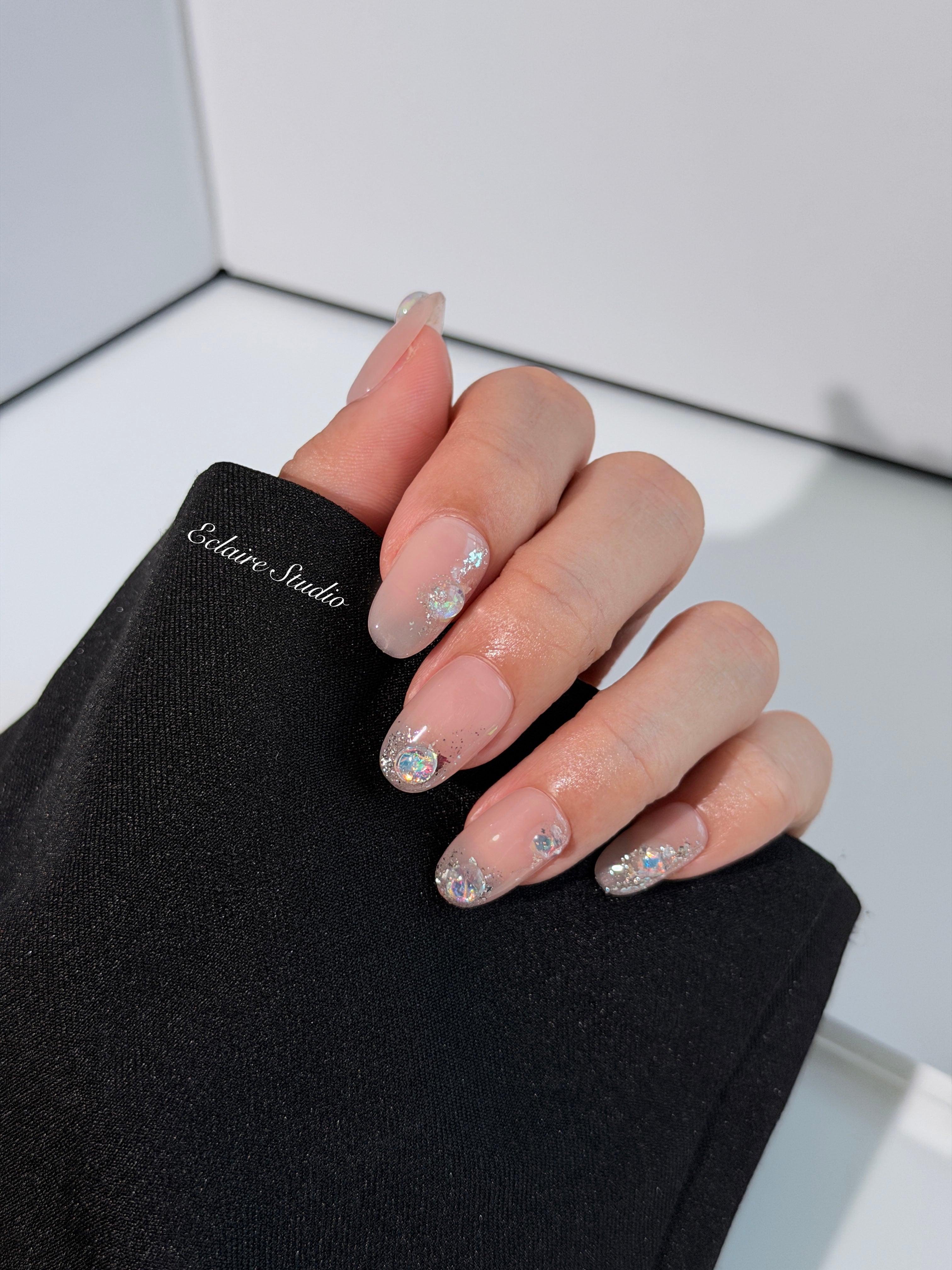 Short milky nude press-on nails with iridescent glitter and 3D crystal droplets, soft winter sugar aesthetic.
