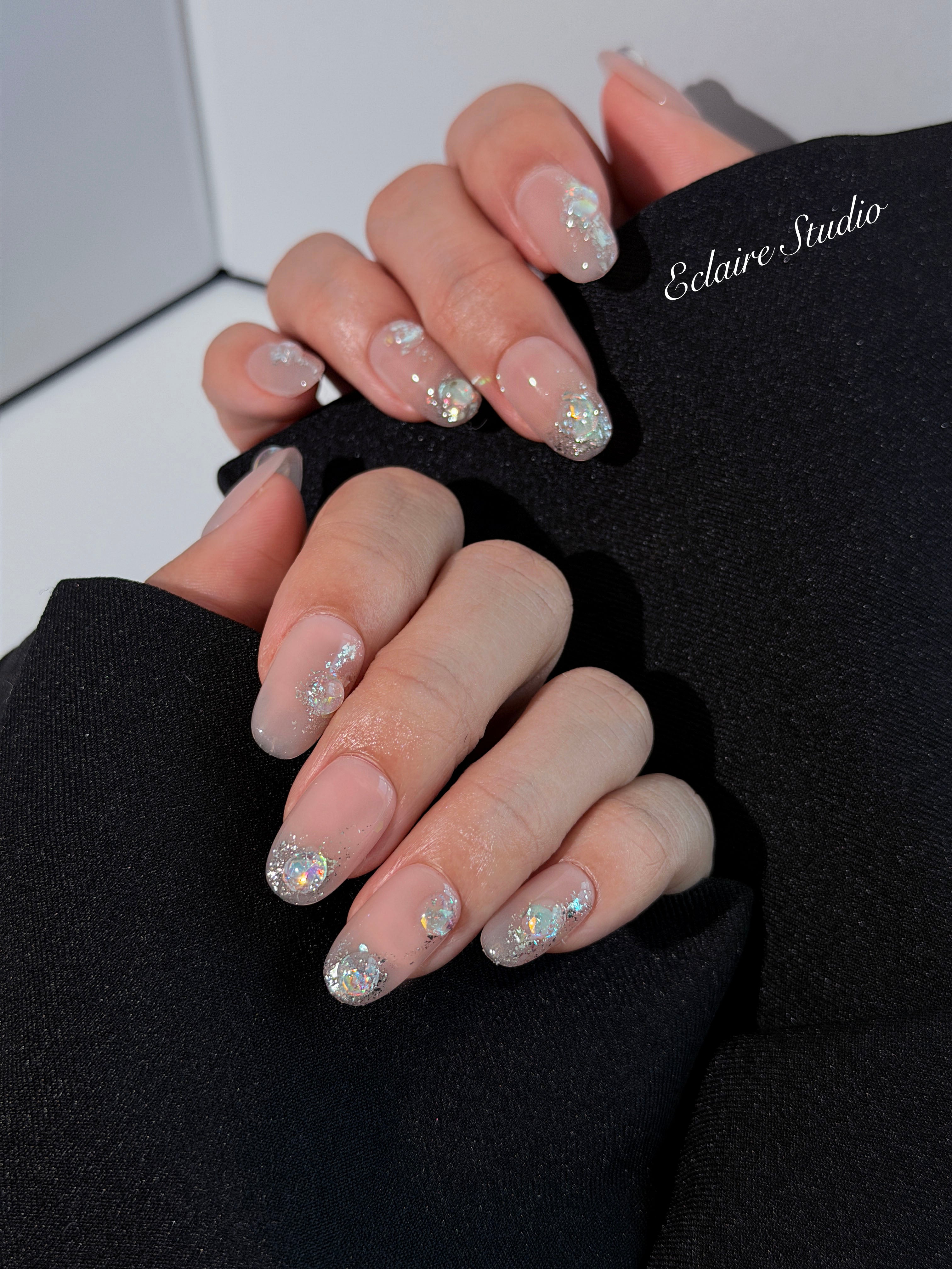 Short milky nude press-on nails with iridescent glitter and 3D crystal droplets, soft winter sugar aesthetic.
