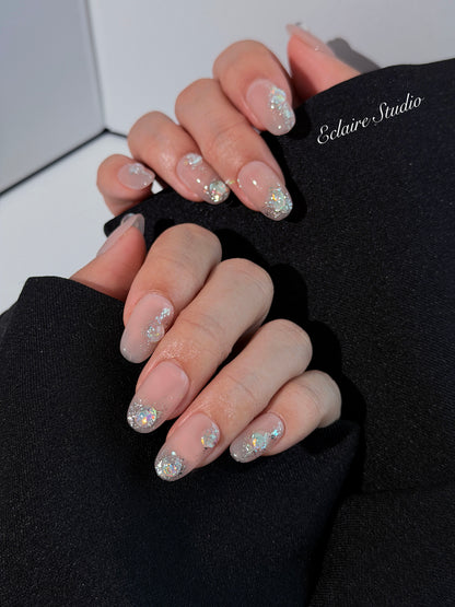 Short milky nude press-on nails with iridescent glitter and 3D crystal droplets, soft winter sugar aesthetic.
