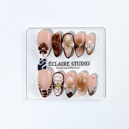 Petal Locket almond press-on nails with nude bases, ivory 3D flowers, brown florals, tortoiseshell, animal-print French tips, pearls, and gold accents.
