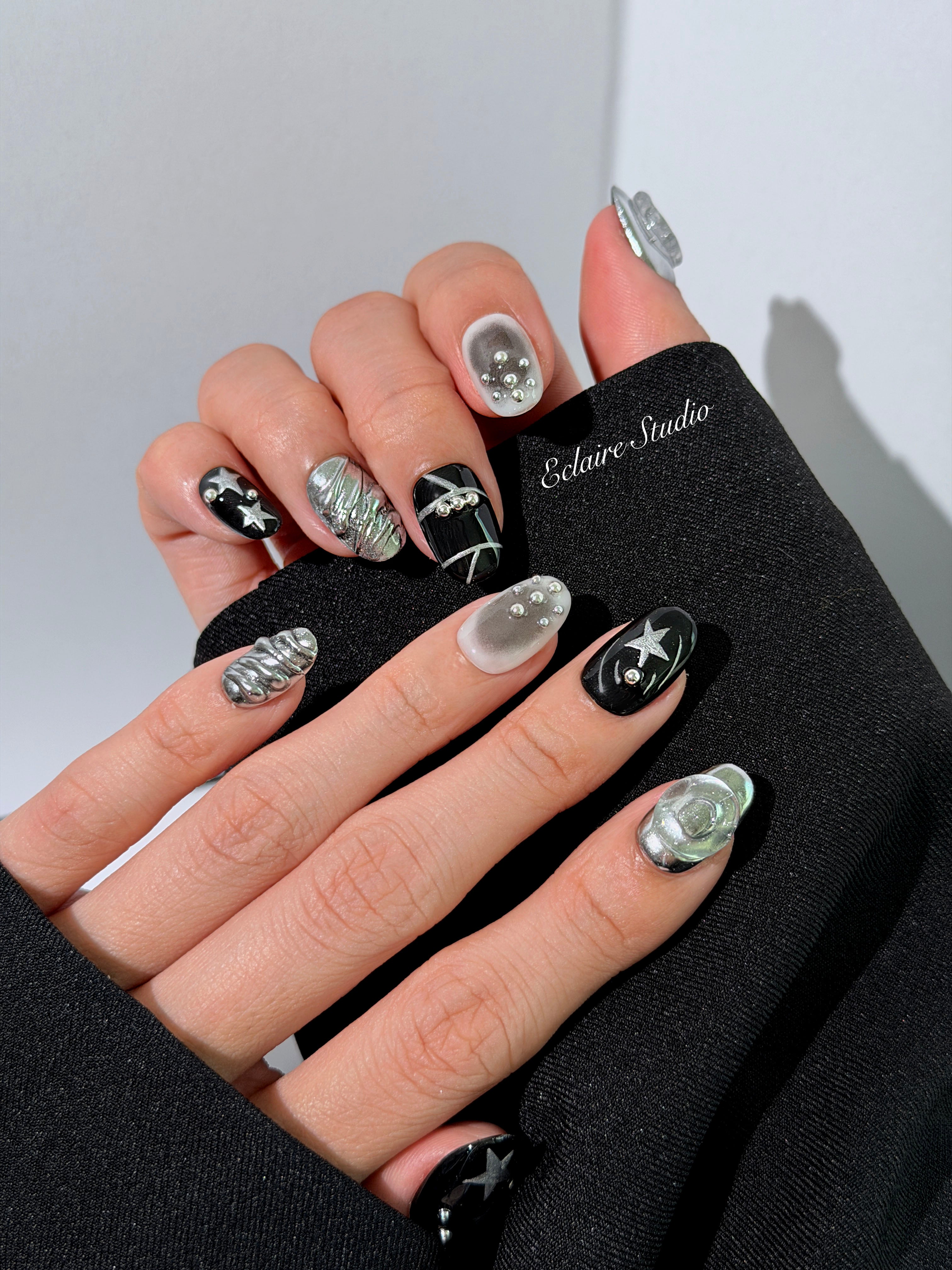 Black and silver press-on nails with 3D chrome swirl accents, star details, and shimmer gradient in a bold winter aesthetic.
