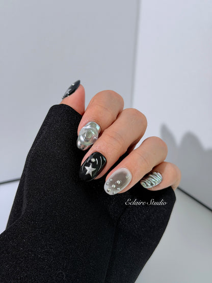 Black and silver press-on nails with 3D chrome swirl accents, star details, and shimmer gradient in a bold winter aesthetic.
