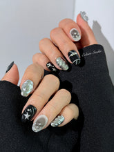 Black and silver press-on nails with 3D chrome swirl accents, star details, and shimmer gradient in a bold winter aesthetic.

