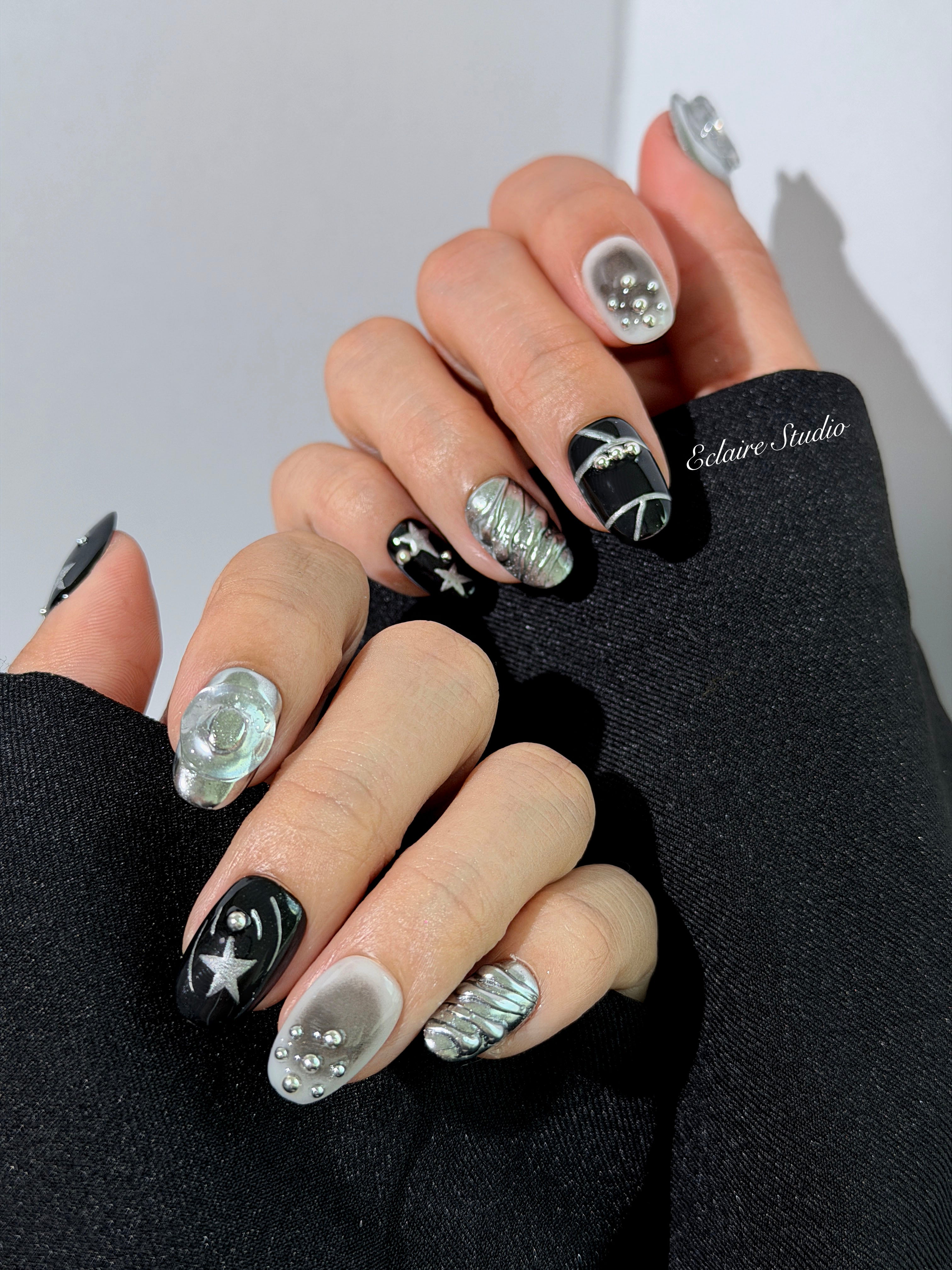 Black and silver press-on nails with 3D chrome swirl accents, star details, and shimmer gradient in a bold winter aesthetic.


