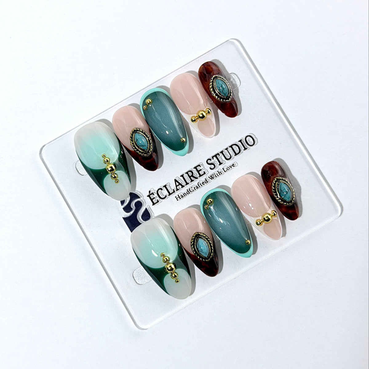 Jasmine’s Secret almond press-on nails with teal and blush bases, tortoiseshell French tips, turquoise-toned oval jewels, gold frames, and gold beads.