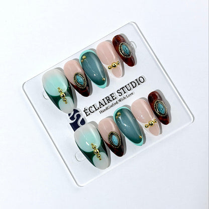 Jasmine’s Secret almond press-on nails with teal and blush bases, tortoiseshell French tips, turquoise-toned oval jewels, gold frames, and gold beads.