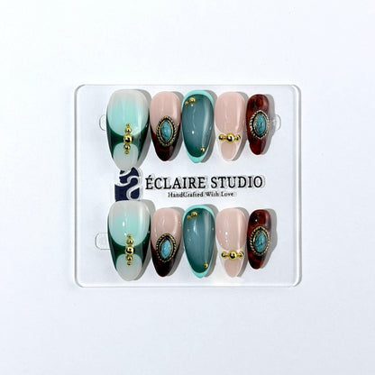 Jasmine’s Secret almond press-on nails with teal and blush bases, tortoiseshell French tips, turquoise-toned oval jewels, gold frames, and gold beads.