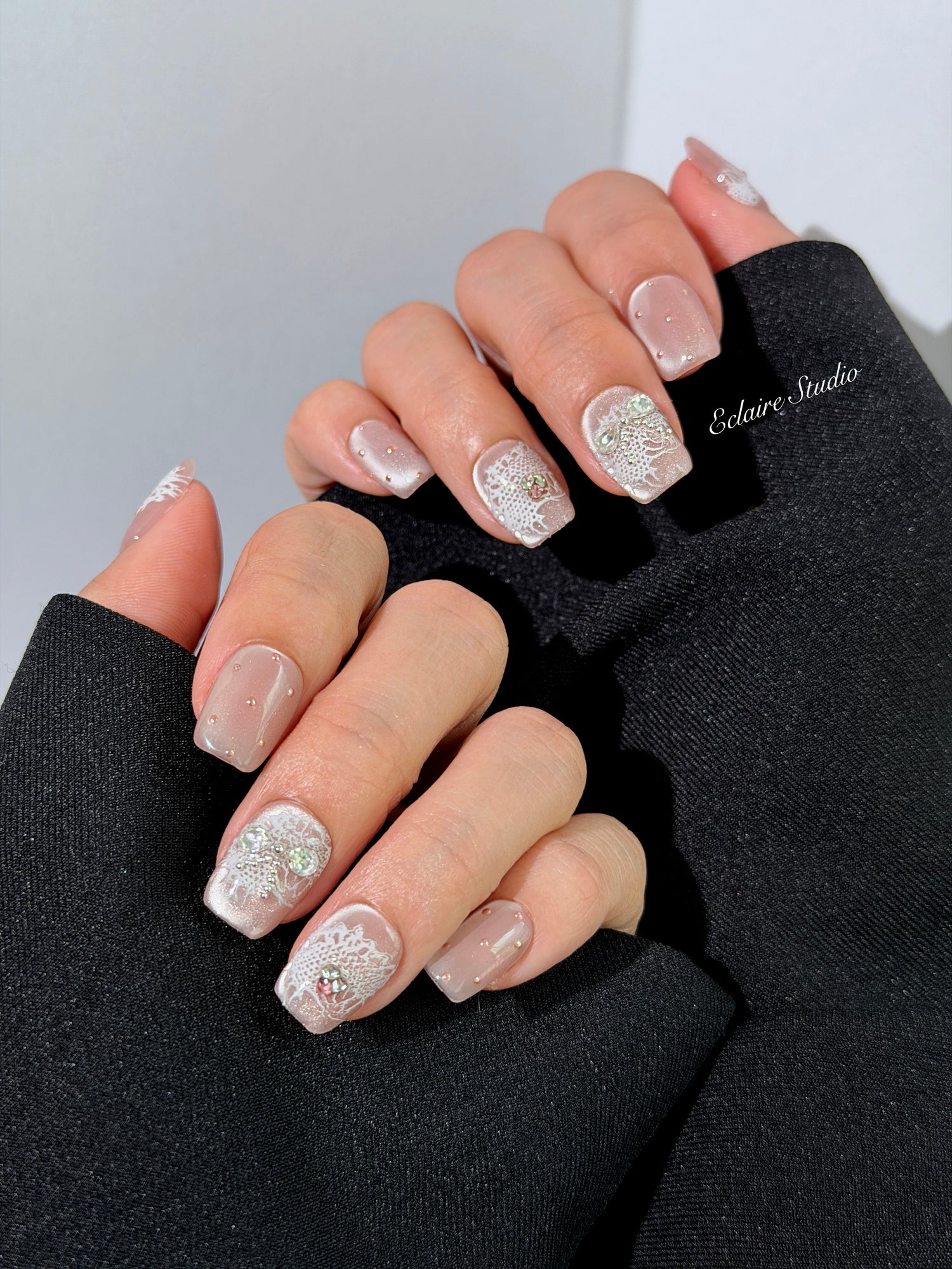 Short coffin pink nude cat-eye press-on nails with lace texture and pearl bow accents in a soft romantic winter style.
