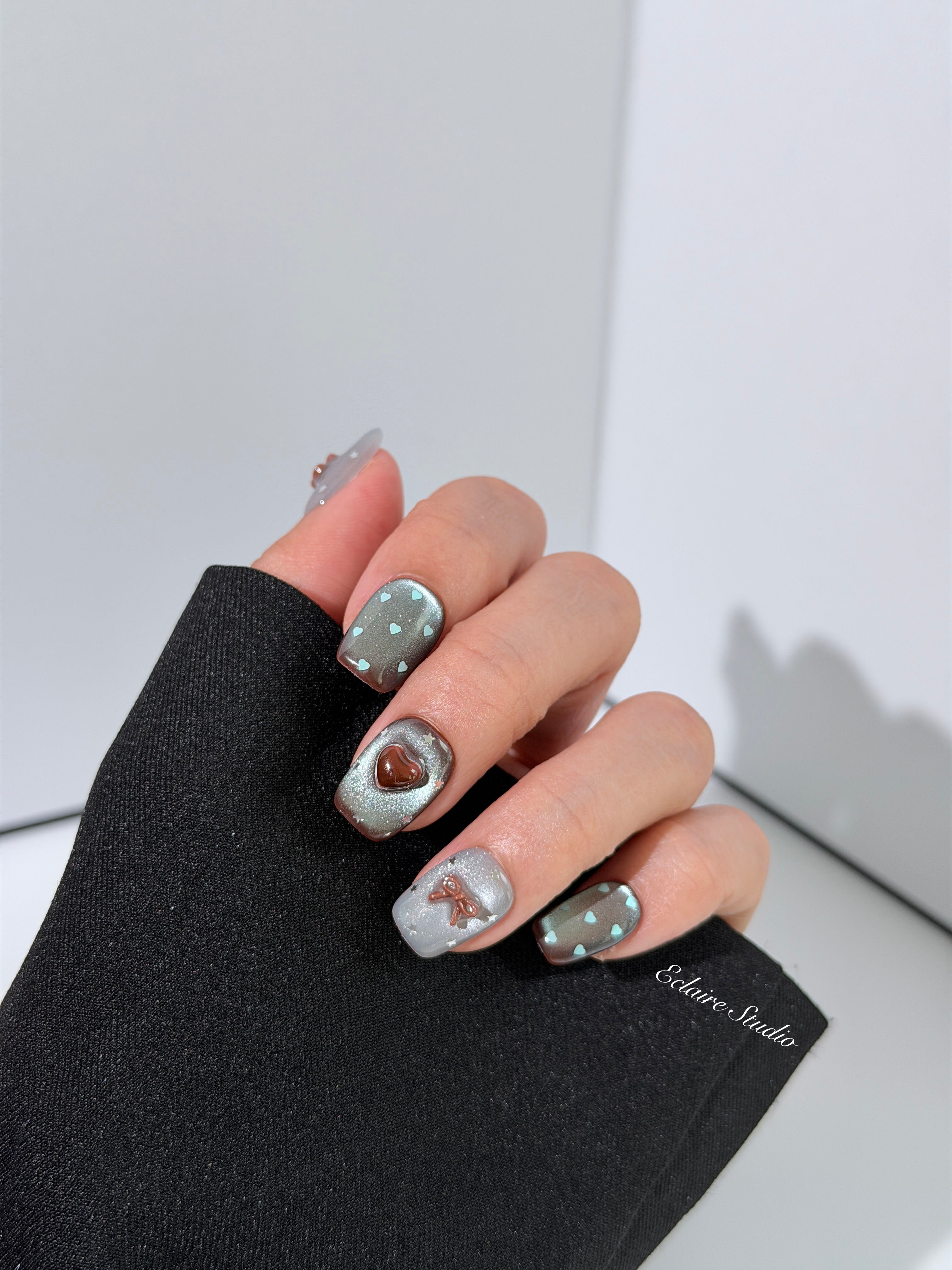 Close-up of short coffin mint shimmer and chocolate brown gradient press-on nails featuring cute hearts, bows, and glitter accents.