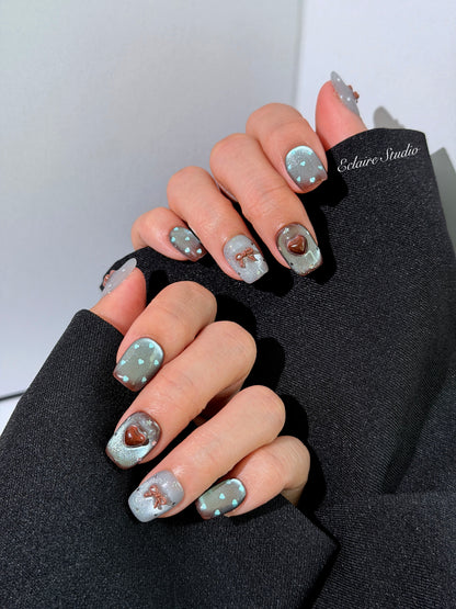 Close-up of short coffin mint shimmer and chocolate brown gradient press-on nails featuring cute hearts, bows, and glitter accents.