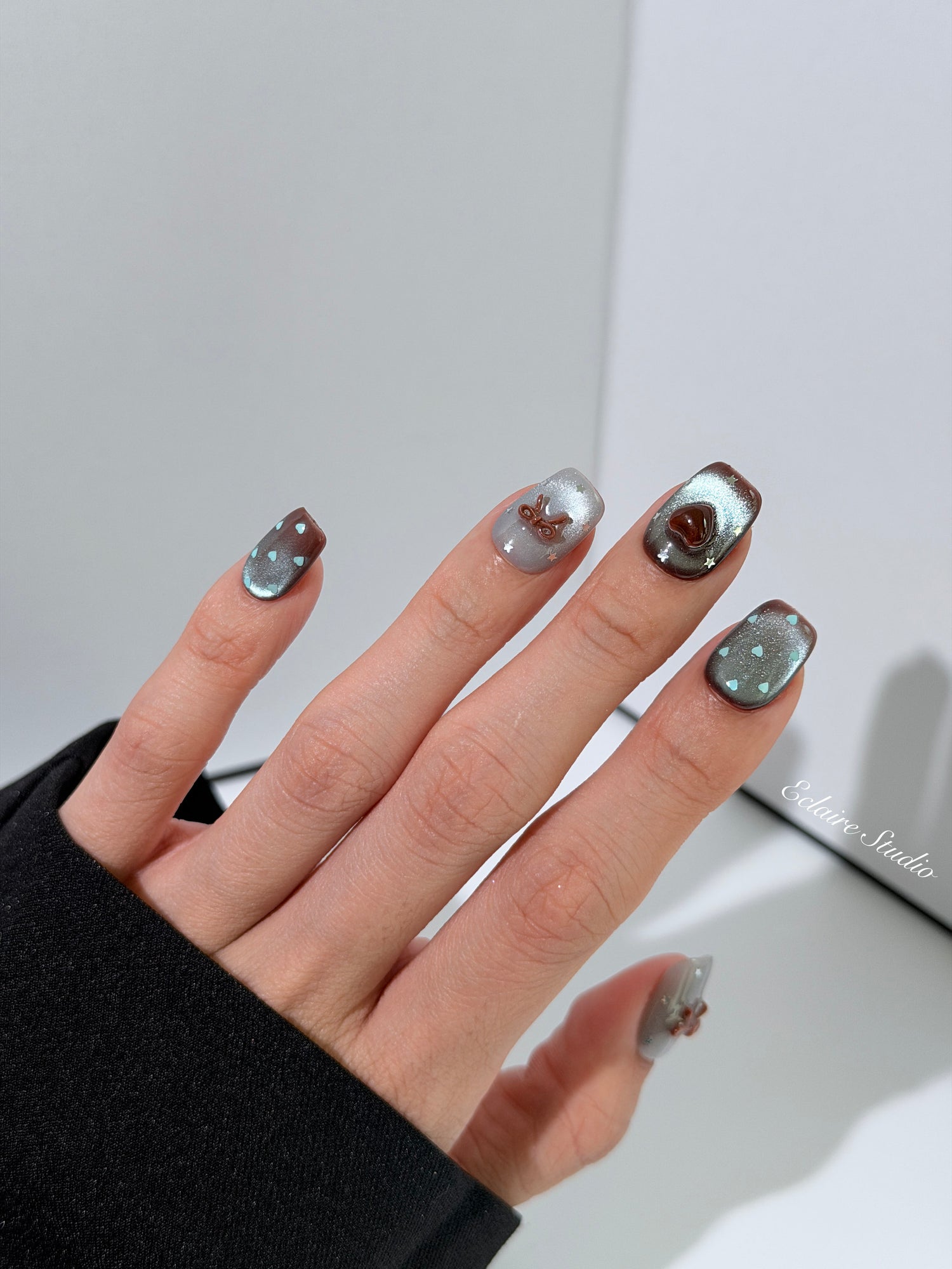 Close-up of short coffin mint shimmer and chocolate brown gradient press-on nails featuring cute hearts, bows, and glitter accents.