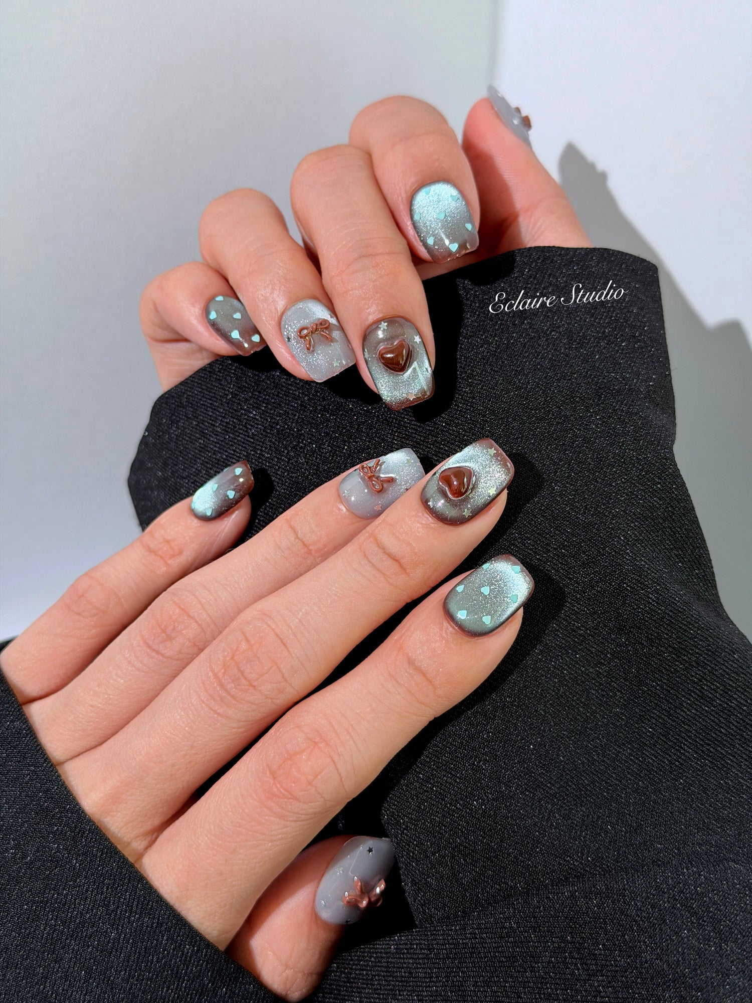 Close-up of short coffin mint shimmer and chocolate brown gradient press-on nails featuring cute hearts, bows, and glitter accents.