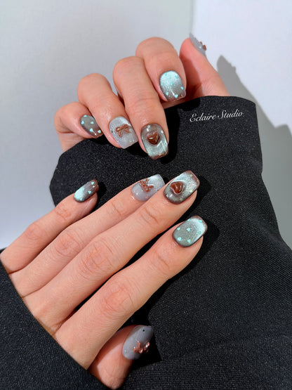 Close-up of short coffin mint shimmer and chocolate brown gradient press-on nails featuring cute hearts, bows, and glitter accents.
